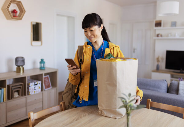 Woman holding smartphone with bag of groceries